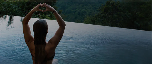 Person making a heart shape with their hands by a pool with a scenic background